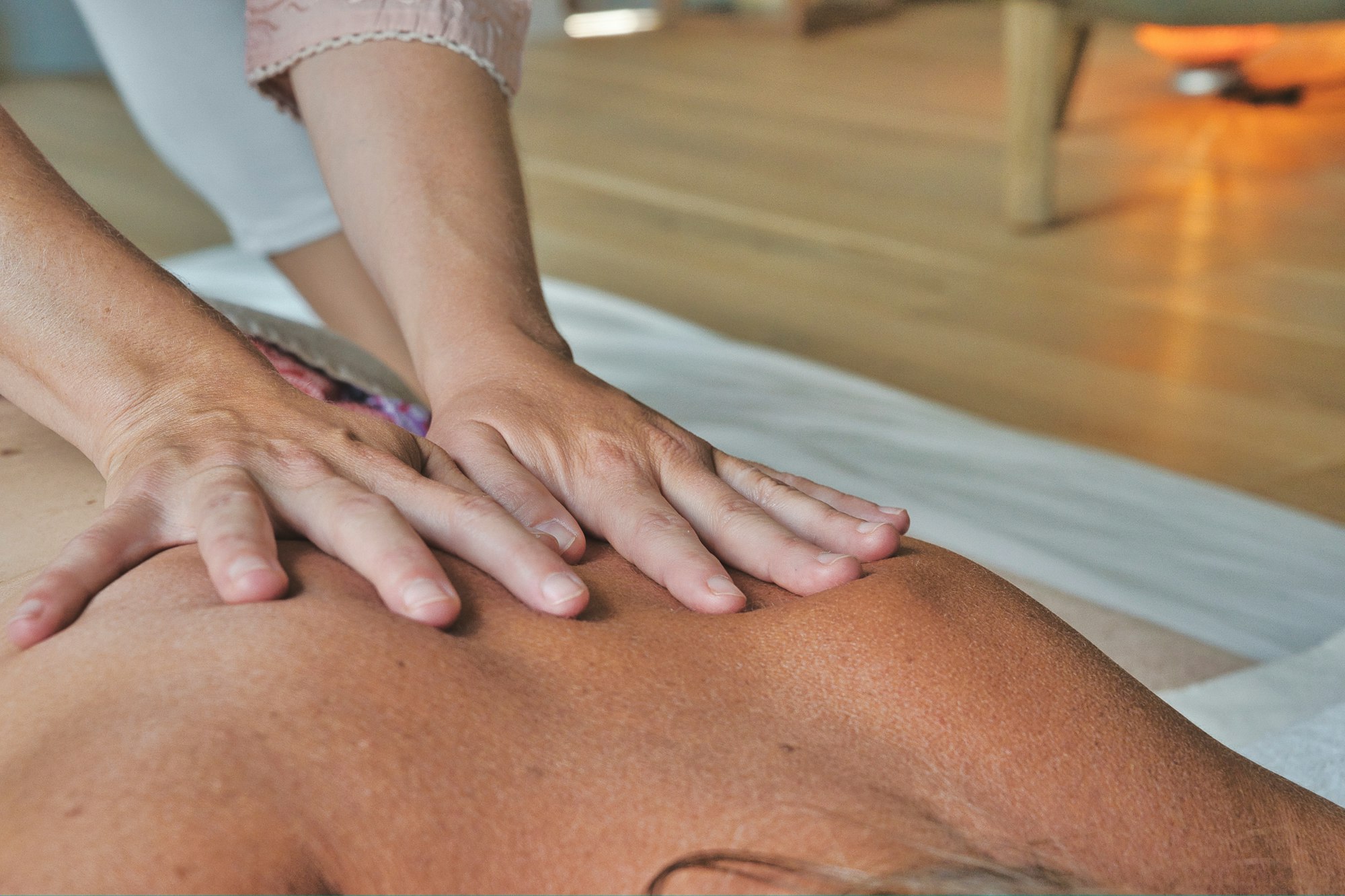 A massage therapist working gently on a client's shoulders in a warm, plant-filled treatment room